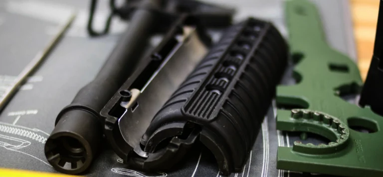 Close-up of disassembled firearm parts, including a black handguard, barrel, and green tools, laid out on a gray gunsmithing mat with white technical diagrams—ideal for practicing skills from POST AR armorer certification St. Louis courses.