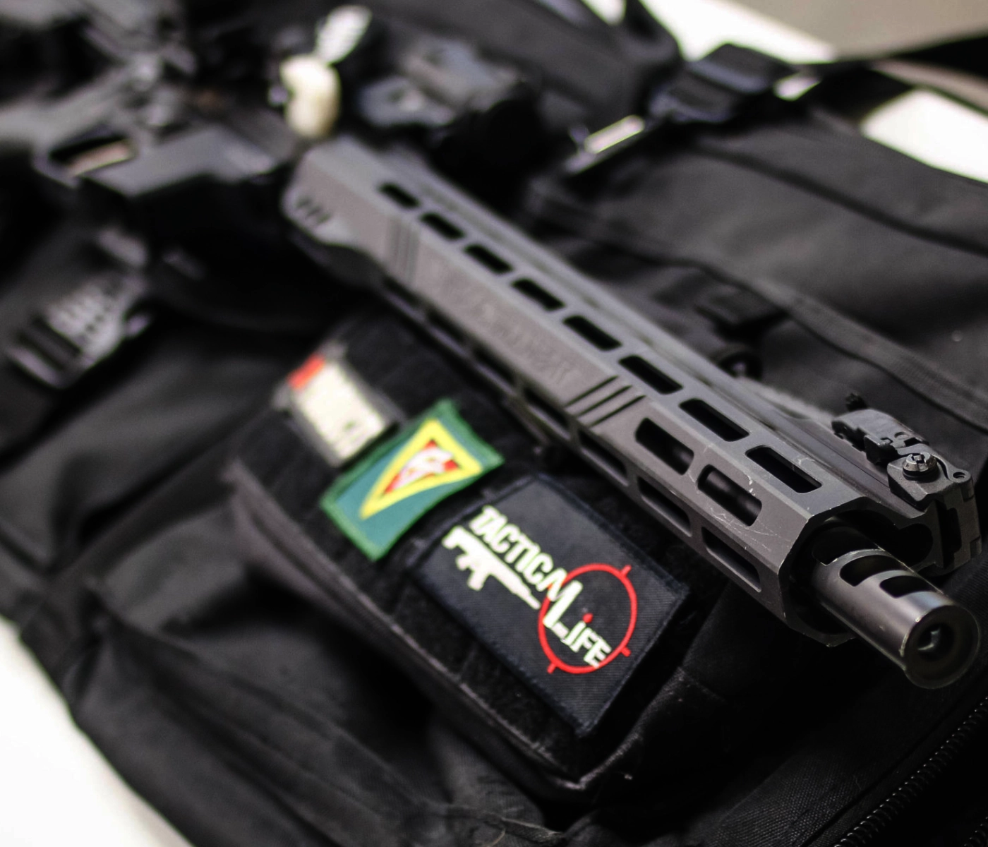 A close-up of a tactical rifle lying on a black bag adorned with colorful patches, including one labeled "TACTICAL LIFE" with a red target—perfect gear for anyone starting their basic rifle course St. Louis.