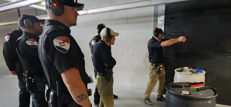 Several uniformed officers wearing headphones observe as one person completes a POST practical pistol qualification at an indoor shooting range in St. Louis; equipment and safety gear are visible in the scene.